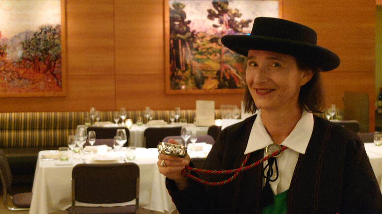 pamela wittman wearing the traditional hat and uniform of les compagnons du beaujolais holds a tastevin in the elegant boulud sud ny dining room